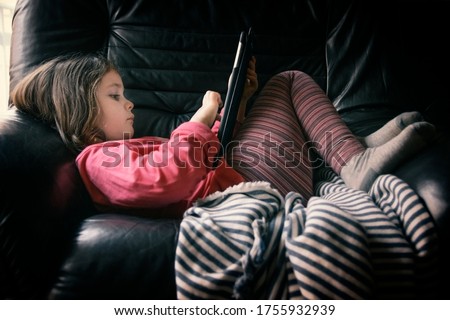 Child girl laying on the sofa reading some online ebooks in a tablet device. Empty copy space for Editor's content.