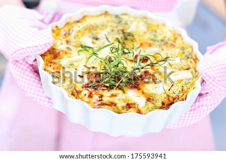 A picture of a spinach quiche hold in oven gloves over pink apron