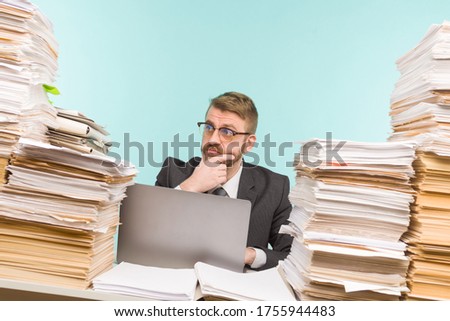 Shocked businessman sitting at the table with many papers in office, he is overloaded with work - image Royalty-Free Stock Photo #1755944483