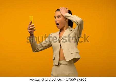 Image of a beautiful shocked young brunette woman posing isolated over yellow wall background using mobile phone. - image