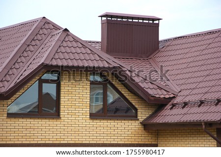 Brown roof of the house with nice windows and a chimney. Close-up. The concept of roofing. Royalty-Free Stock Photo #1755980417