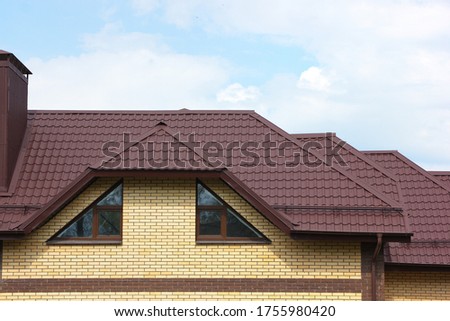 Brown roof of the house with nice windows and a chimney. Close-up. The concept of roofing. Royalty-Free Stock Photo #1755980420