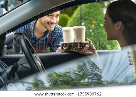 Waiter giving hot coffee cup with disposable tray and bakery bag through car window to customer at drive thru service station. Drive thru is popular service after coronavirus covid-19 pandemic. Royalty-Free Stock Photo #1755989762