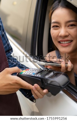 Asian woman customer make mobile payment contactless technology to waiter in drive thru food service while pickup coffee and bakery. Drive through is more  popular after coronavirus covid-19 pandemic.