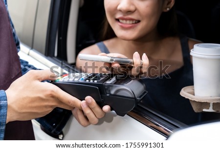 Asian woman customer make mobile payment contactless technology to waiter in drive thru food service while pickup coffee and bakery. Drive through is more  popular after coronavirus covid-19 pandemic.