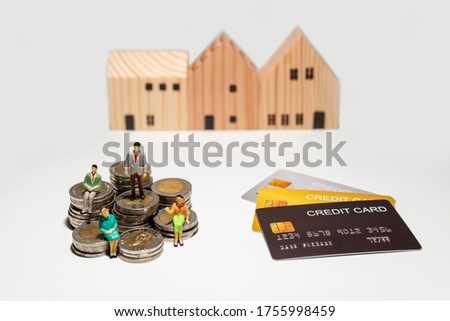 Miniature figure standing and sitting on stacked coin with credit card and wooden house isolated on white background, concept planning savings money and credit for buy a house.