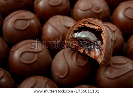 Sweet confectionery and candy indulgence concept theme with close up on a bitten cherry filled chocolate praline on top of many other delicious pralines with copy space Royalty-Free Stock Photo #1756011131