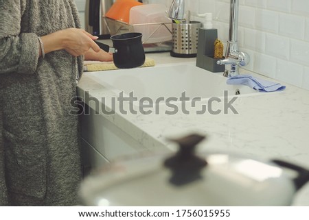 Woman holding pouring water from faucet in pan 
