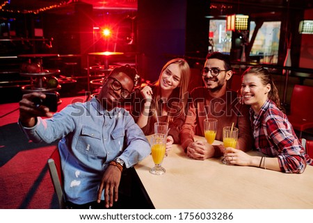 Four happy friends in casualwear making selfie by table in the bar while having drinks after watching bowling game of their favorite team