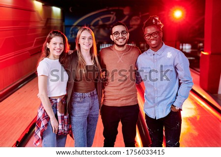 Row of young cheerful friends of various ethnicities standing in front of camera on background of bowling tracks at leisure center