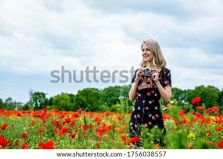 Blonde girl in beautiful dress with vintage camera in poppies field in summer time