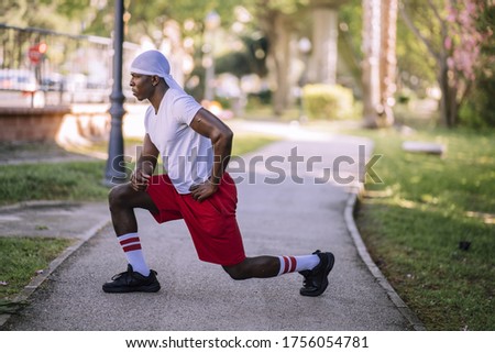 A shallow focus shot of an African-American male in a white shirt stretching at the park
