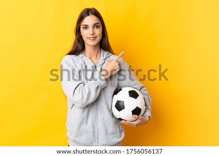 Young football player woman isolated on yellow background pointing to the side to present a product