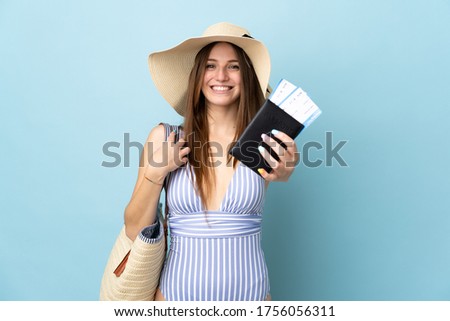 Young caucasian woman in summer holidays holding passport isolated on blue background with happy expression