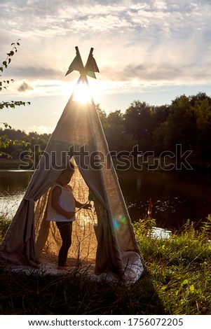 Girl at sunset in nature. Wigwam by the lake. New home in a hut. CHILDREN'S GAMES. High quality photo