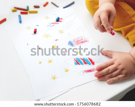 Toddler sits on windowsill and draws colorful fireworks. Child's picture to 4th of July celebration. Independence Day of USA symbol.