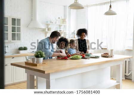 Happy mixed race multinational family with daughters prepare vegetable organic fresh salad, enjoy pastime cooking process in cozy kitchen, healthy eating, parents teach kids, weekend at home activity Royalty-Free Stock Photo #1756081400