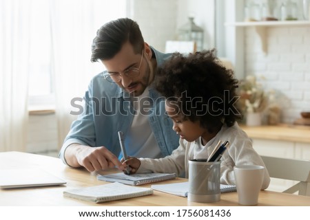Loving stepdad or tutor helps understand arithmetic task provide care and patience during homeschooling with little mixed-race African daughter kid girl. Child development, schoolwork at home concept Royalty-Free Stock Photo #1756081436