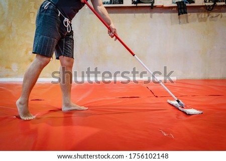 Unknown caucasian man cleaning tatami mats at MMA or BJJ or Judo wrestling martial arts gym using mop to swipe and disinfect due to coronavirus pandemic or bacteria fungus preventing infection