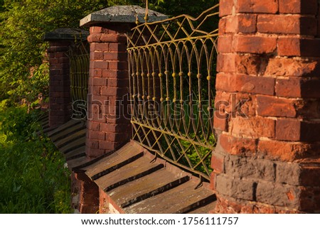 Fence of an old orthodox church from time-damaged red brick with metal forged spans