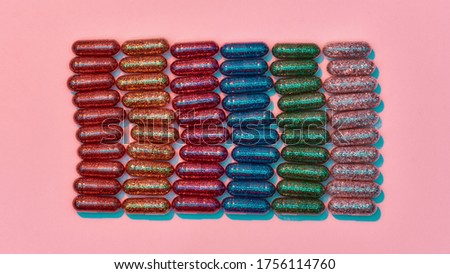 Creative concept with many colorful glitter pills lying in rows isolated on pastel pink background. Minimal style, art concept. Top view. Horizontal shot