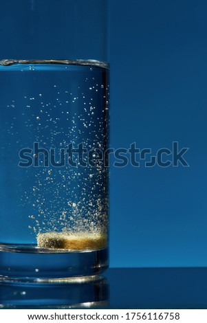 Close up of glass of water with effervescent aspirin tablet, pill in it isolated over blue background. Health concept. Vertical shot