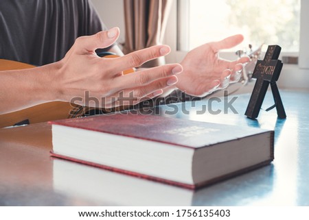 Hands lifting up and praising to God with Holy Bible and symbol of cross on the table, together with guitar.