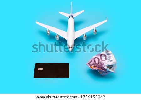 a plane, a crumpled bill, and a card on a blue background. The photo symbolizes the choice and rejection of paper money in favor of plastic cards for paying for a plane ticket