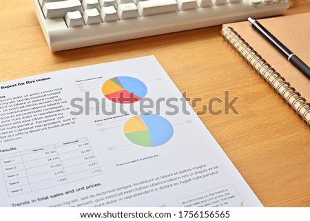 ﻿There is a dummy paper with a white keyboard and a pie chart written on it, along with a notebook and pen.