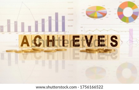 ACHIEVES the word on wooden cubes, cubes stand on a reflective surface, in the background is a business diagram. Business and finance concept