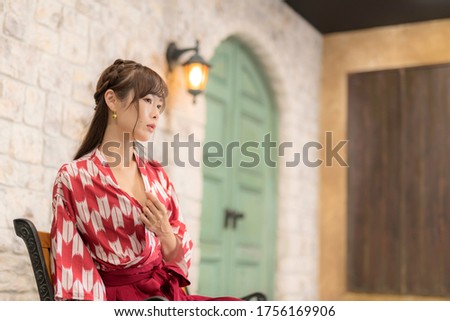 
Japanese woman in kimono sitting on chair by brick wall