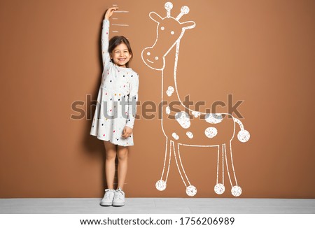 Little girl measuring height and drawing of giraffe near brown wall Royalty-Free Stock Photo #1756206989