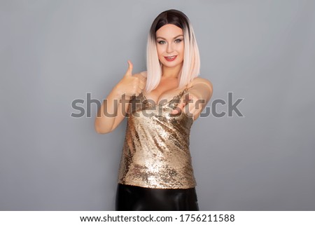 Young stylish blonde woman dressed in a golden top and leather pants posing on a gray background in the studio