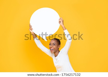 Cheerful happy young African American woman smiling and holding speech bubble with empty space for text overhead isolated on yellow background