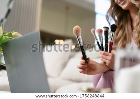 Attractive female make-up artist streaming on a laptop. Beauty blogger talking about various / different makeup brushes and shows them to her subscribers online