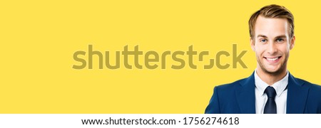 Wide composition photo - confident businessman in blue suit and tie, isolated against yellow color background. Smiling caucasian man at studio picture. Copy space for some text.