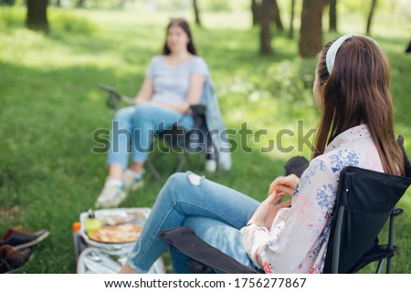 Social distancing. Girls Friends chilling among trees at picnic with social distance in summer park. Leisure activity together in new normal, safety gatherings. Young woman relaxing Royalty-Free Stock Photo #1756277867