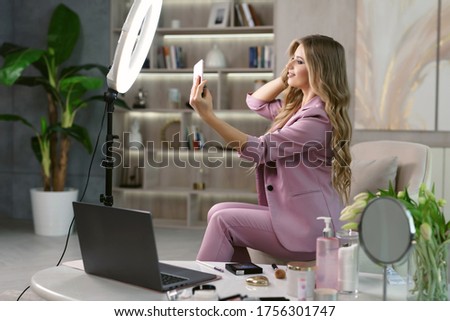 Young attractive woman famous blogger taking a selfie for a social network using a smartphone and a ring lamp. Girl fooling around on camera.