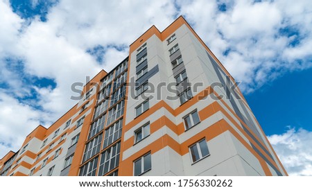 Modern orange-and-white multi-storey building against a blue sky with clouds, photo from bottom to top