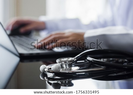 Female doctor in white lab coat typing on laptop computer with notebook and medical stethoscope on the desk at workplace. Medical technology ,Electronic health record system (EMR) concept
