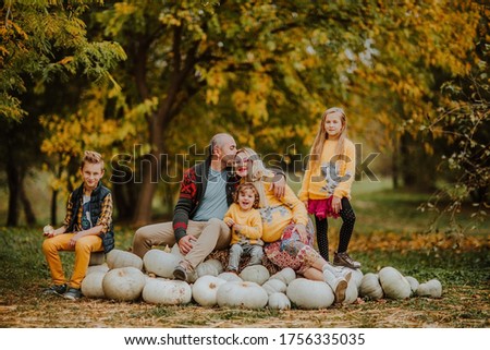 Big cute family of five sitting on a white pumpkin's hill and smile. Autumn background.