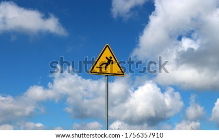 Yellow triangular falling danger sign against blue sky with fluffy clouds on background