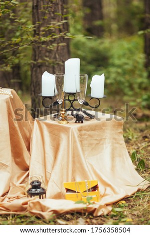 Wine glasses and candlesticks are arranged on tables in the forest.