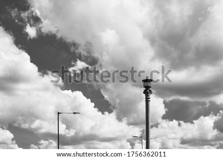 Monochrome, high contrast view of a very old, gas fired street lamp seen together with two recently installed, low energy street lights against a summer sky.