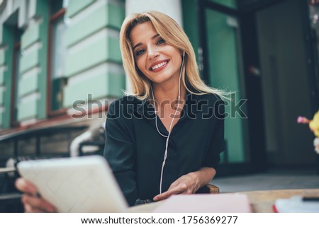 Portrait of pretty female millennial with cute smile and white teeth looking at camera spending time for music hobby, happy blonde woman in electronic headphones listening positive audio playlist