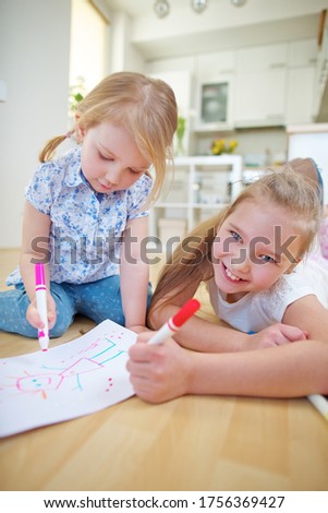 Two girls draw a picture together with felt-tip pens at home