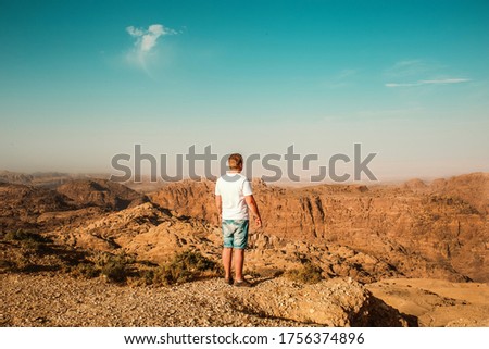 A man on top of a mountain in bright Sunny summer weather looks at the view from the mountains fresh air and wind, a young man of athletic build climbed to the top of the cliff