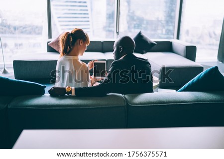 Back view of diverse male and female lawyers reading text publication on mockup touch pad with copy space area for business information, executive traders using blank gadget for making online booking
