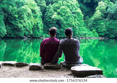 rear view of a romantic gay couple sitting in a beautiful landscape with lake and mountains in a calm moment Royalty-Free Stock Photo #1756376534