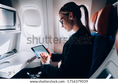 Caucasian female passenger reading eBook during international flight in business class of jetliner, successful woman using wifi internet connection on board for watching movie during free time Royalty-Free Stock Photo #1756379039